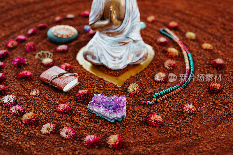 Close up of a sacred meditation ritual still life on red-brown soil with a Amethyst and a white golden Buddha with various spiritual objects